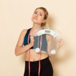 front view young female sport outfit holding scales light white wall fit body sport beauty health exercises