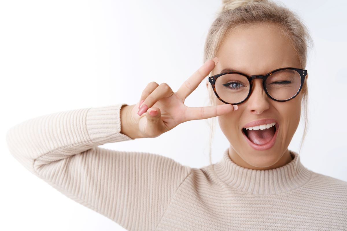 hey smile you portrait cheeky cute glamour blond woman glasses combed hair sweater winking happily showing peace victory gesture as fooling around being optimistic