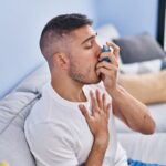 young hispanic man using inhaler sitting sofa home